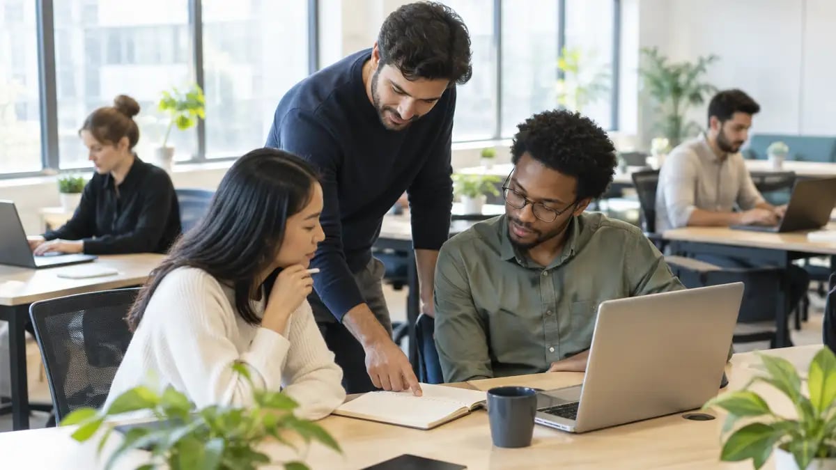 An offshore team leader guiding two colleagues at their desks in a bright, well-run office