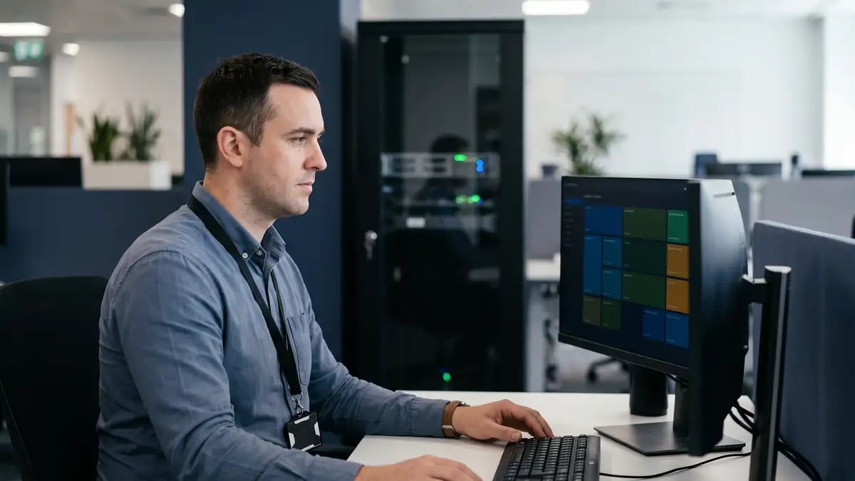 IT security engineer working at a secure workstation with an access badge, server cabinet behind