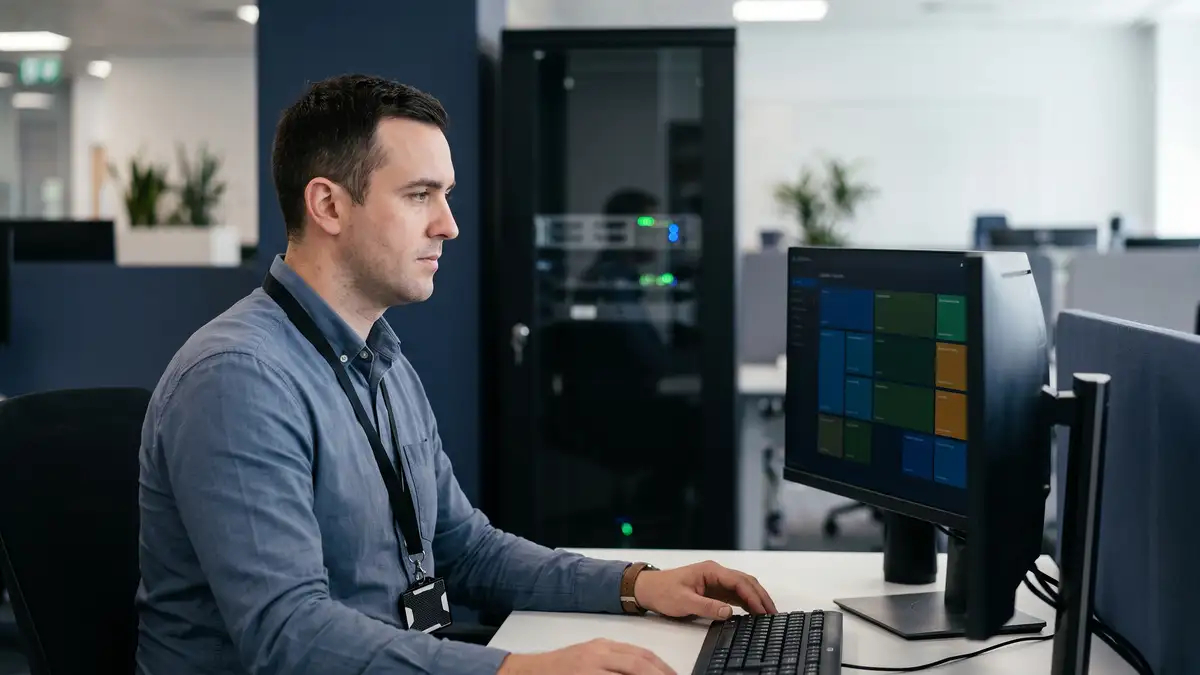 IT security engineer working at a secure workstation with an access badge, server cabinet behind